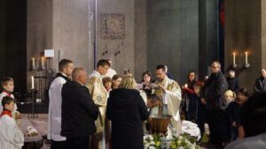 An adult's batism depicting a concelebrated sacrament with with liturgical decor attended by family and friends. water is being poured over a man bending his neck above the baptismal fountain