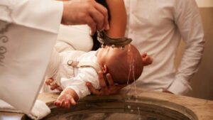 baptism of a baby in a catholic context water being poured over a baby held by the mother with the father standing by